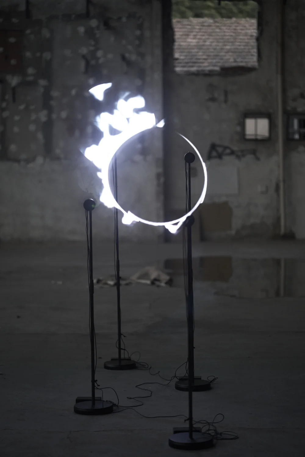 In a disused industrial hall with bare concrete walls, four propellers on stands trace a blazing white ring in mid-air, like an eclipse.