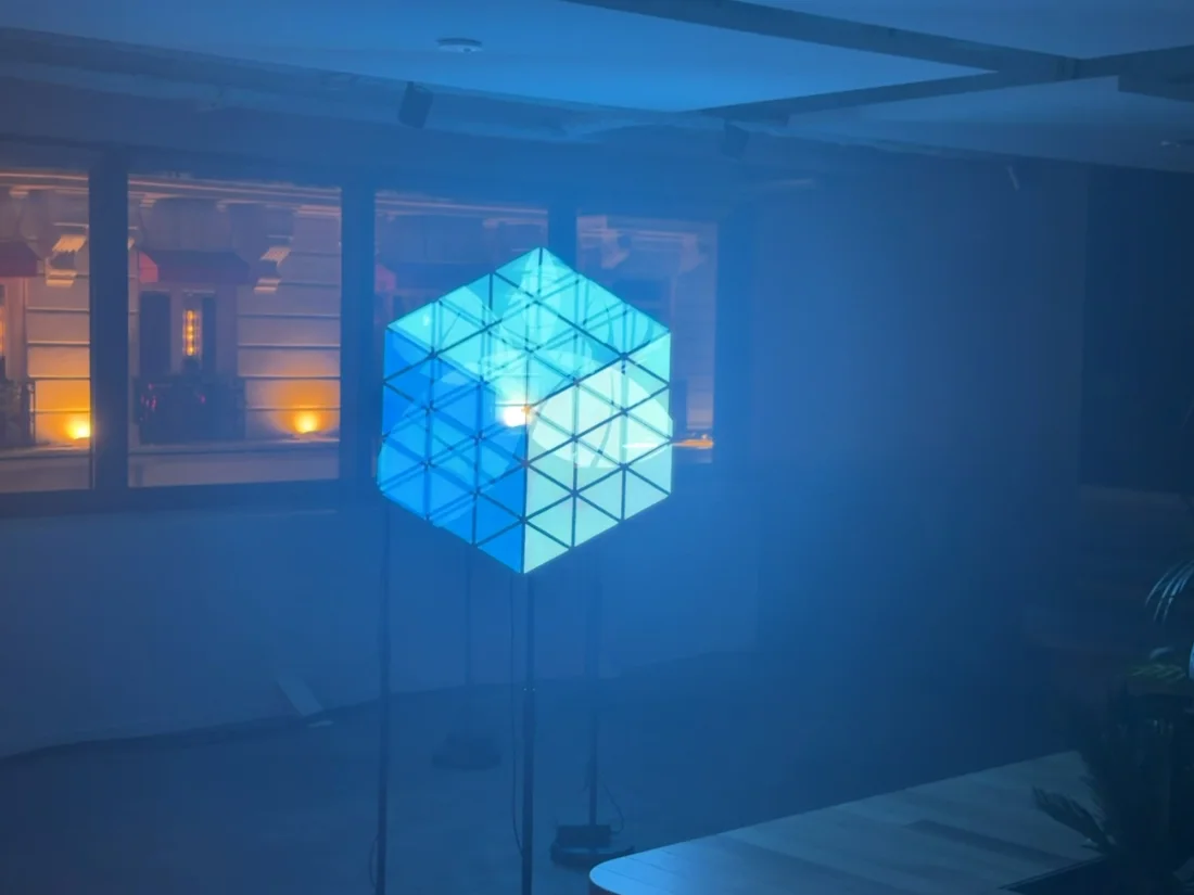 In an office bathed in blue, four propellers recompose a turquoise cube in threads of light, suspended in the middle of the room.