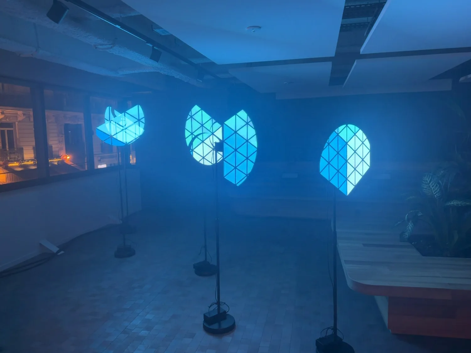 Four propellers on stands in a blue-lit office, each carrying a fragment of light that only comes together from one precise spot in the room.