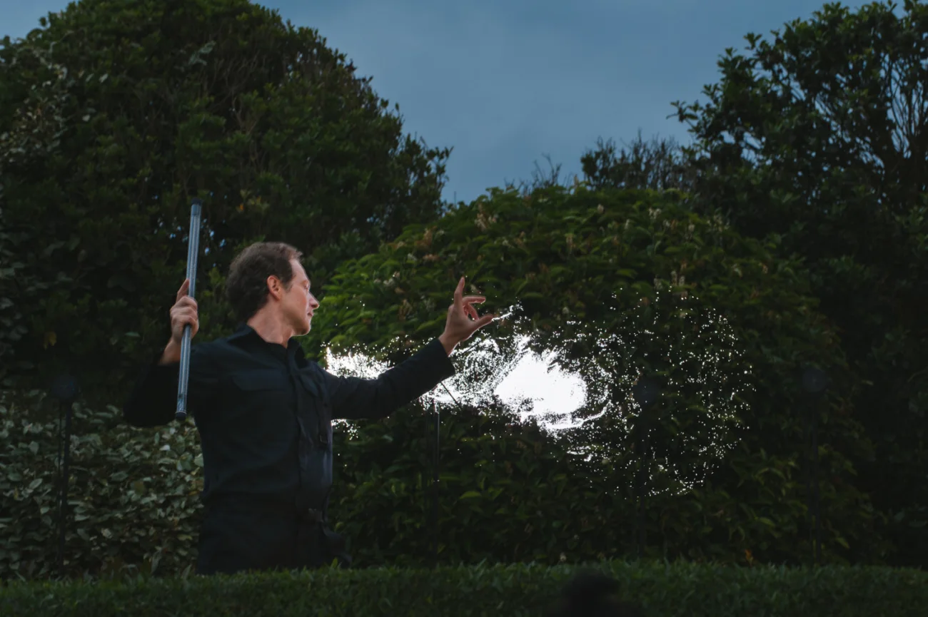 En extérieur à la tombée du jour, le magicien fait apparaître une masse de lumière blanche dans la végétation.