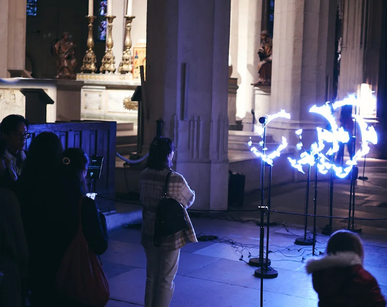 Anamorphose : plusieurs hélices alignées dans une église composent une forme lumineuse bleue devant le public.