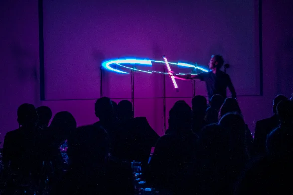 Performance en salle : une hélice trace un anneau lumineux bleu devant une table de convives.